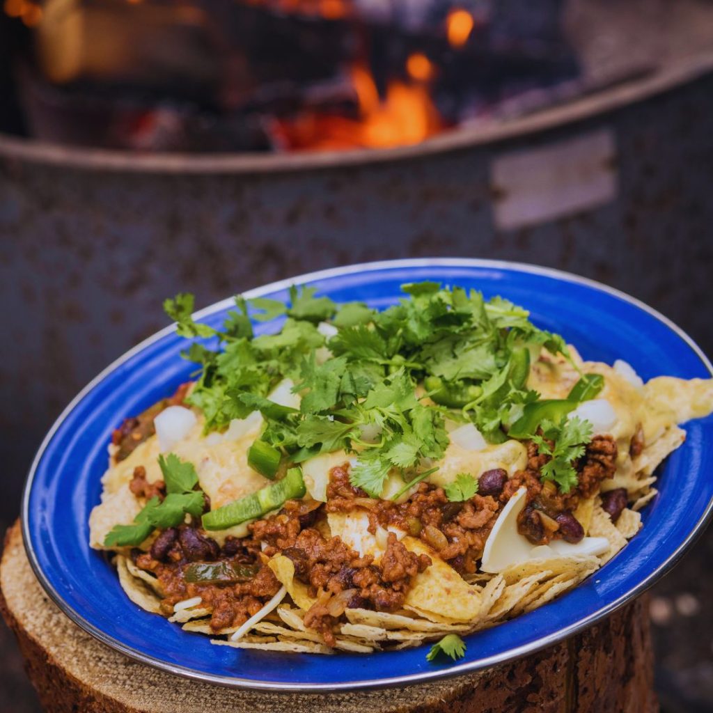 nachos in a blue bowl in front of a campfire